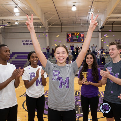 A group of five high school students celebrating on a basketball court, with the central girl in a gray 'dark heather grey Letterman style t-shirt making peace signs with both hands. The gym has purple and gold accents, and confetti is falling.