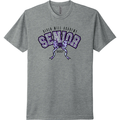 A dark heather gray short-sleeve t-shirt with a purple and glittery silver graphic on the chest reading 'River Mill Academy Senior 2027' with a bow design.